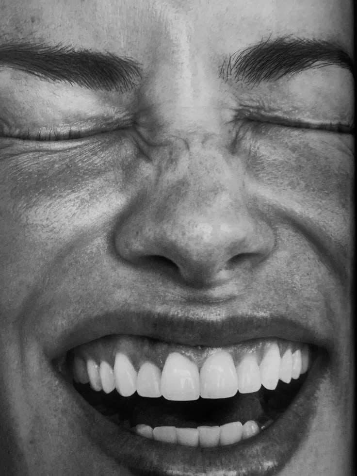 Black-and-white close-up of a face laughing with eyes closed and teeth showing.