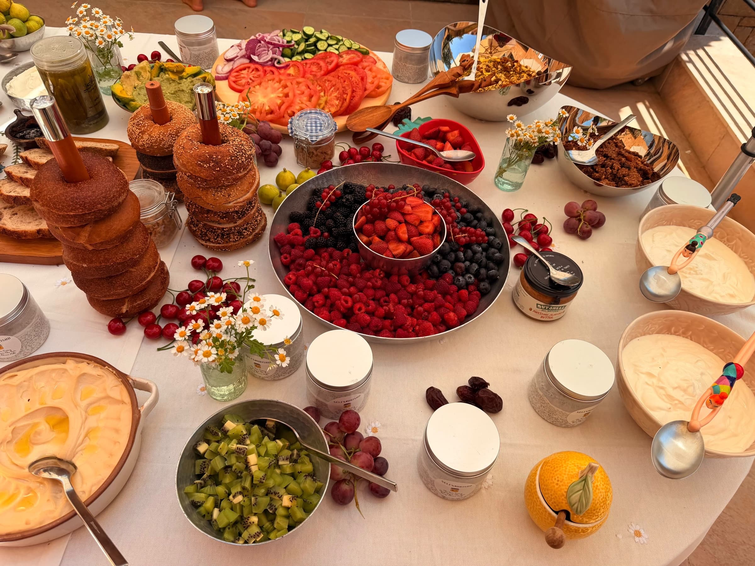 A wide metal platter of raspberries, blackberries, blueberries and strawberries beside stacked sesame bagels