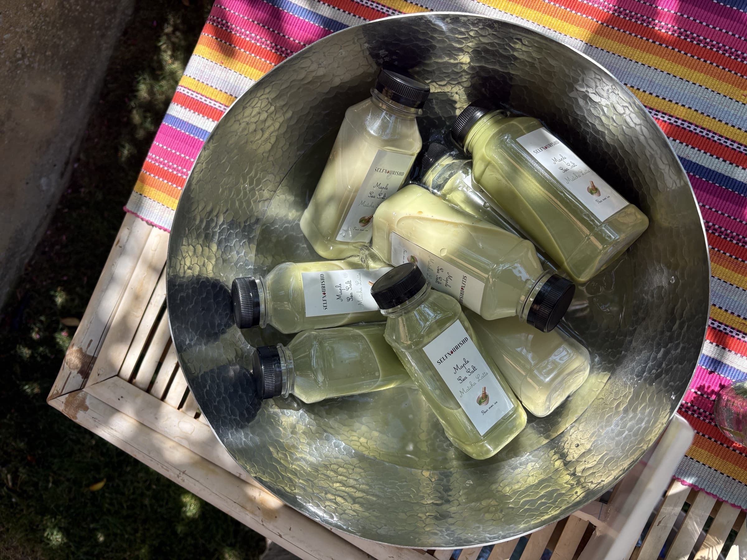 The printed "Hydrate and Glow" beverage menu propped in an ice bucket of bottled drinks under a fern