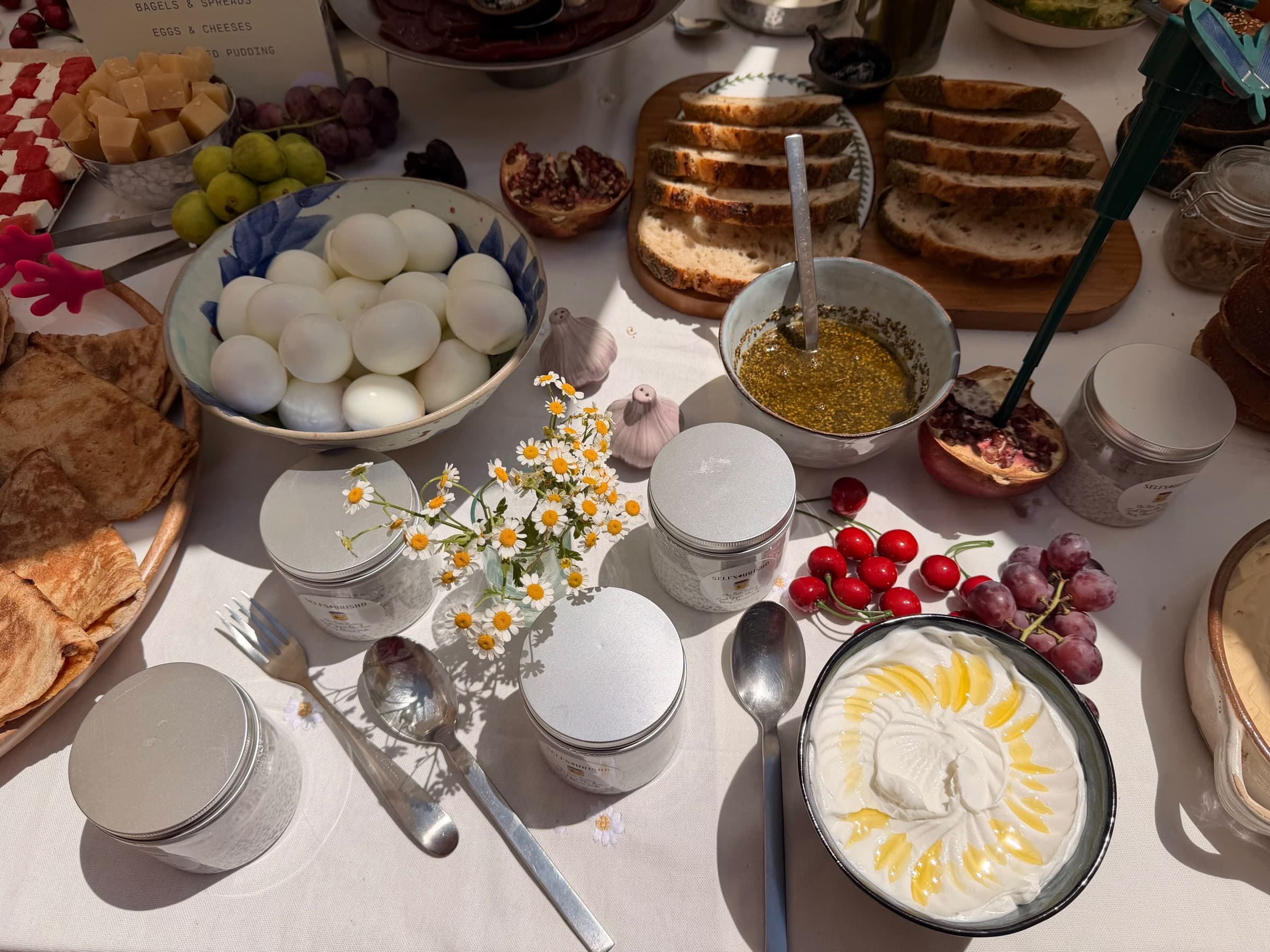 A bowl of boiled eggs, labneh drizzled with olive oil, za'atar in oil and labelled chia jars on white linen