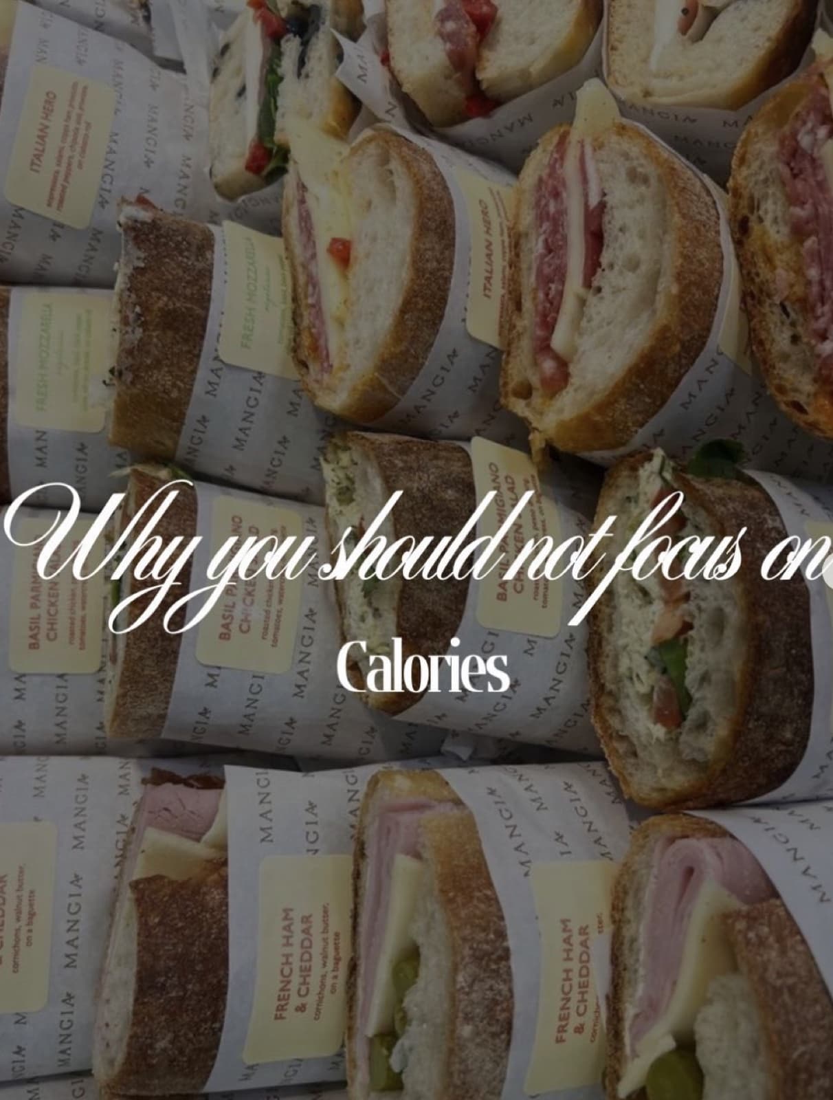 Rows of halved deli sandwiches wrapped in labeled paper, arranged in a grid
